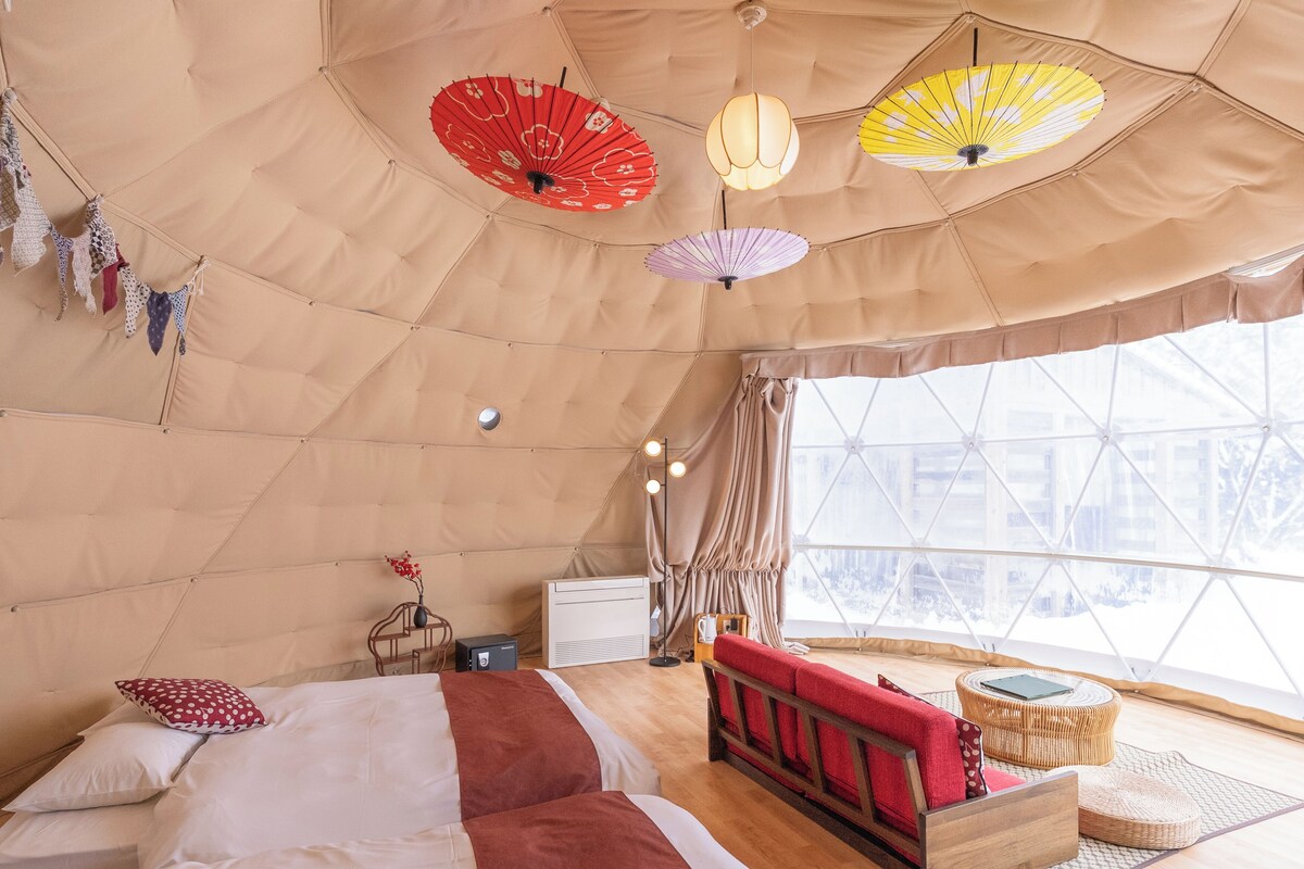A tented room with a bed, a red sofa, a small table, and a window with a view.