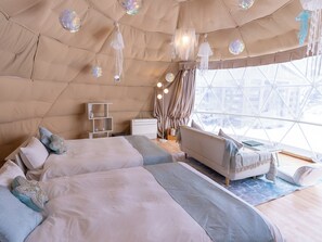 Une pièce confortable, de style tente, bien éclairée, avec un lit, un coin salon et une vue sur l’extérieur grâce à une grande fenêtre.