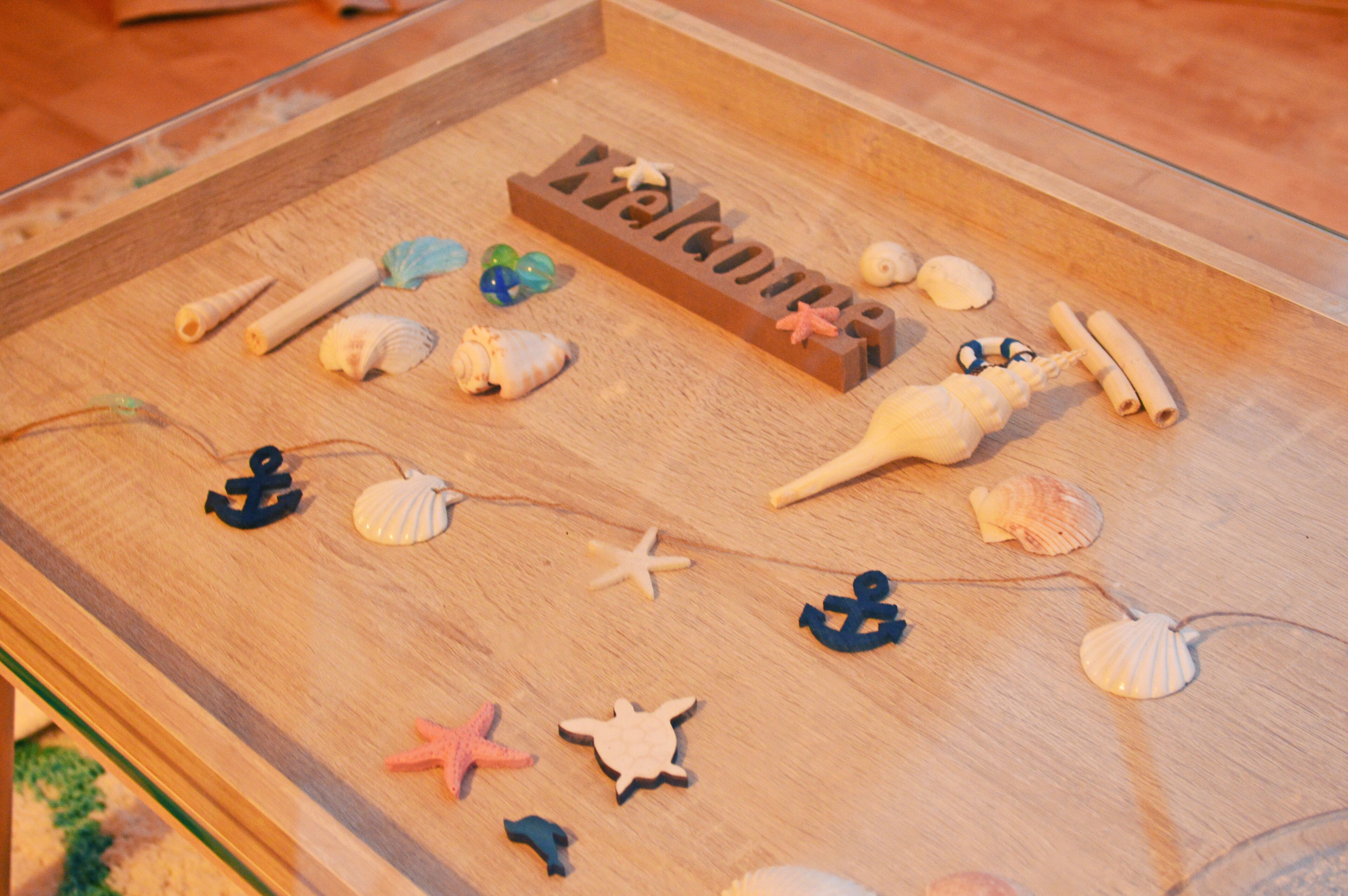 Una tabla de madera con la palabra 'Welcome' y diversas conchas marinas y estrellas de mar.
