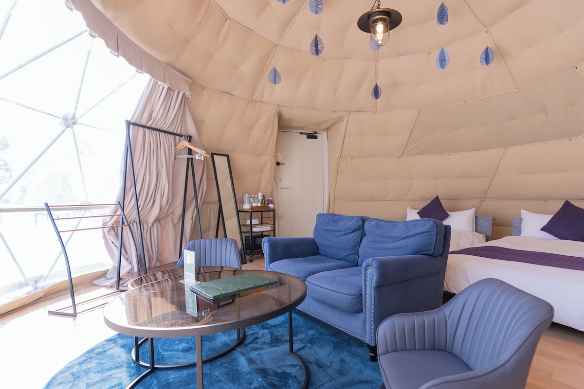 A tented accommodation with a bed, a sofa, a coffee table, and a chair.