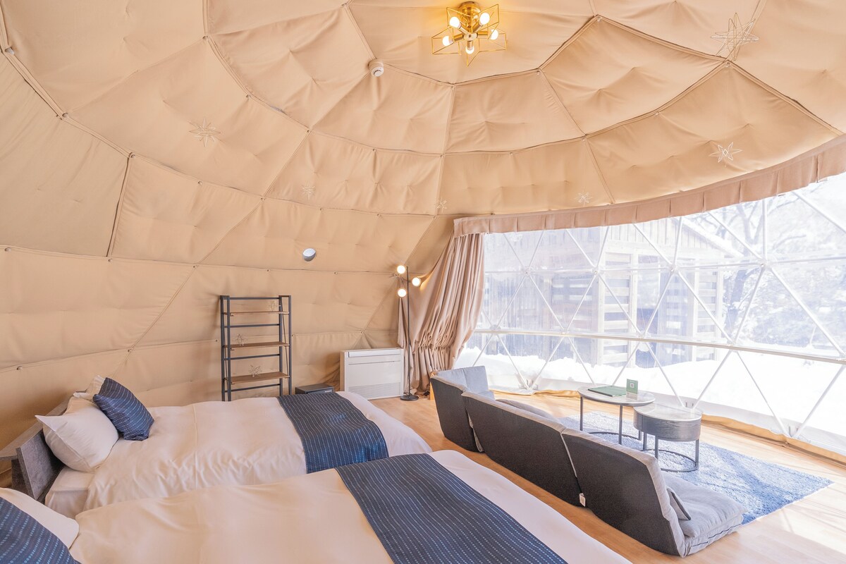 A tented room with two beds, a small table, and a chair.