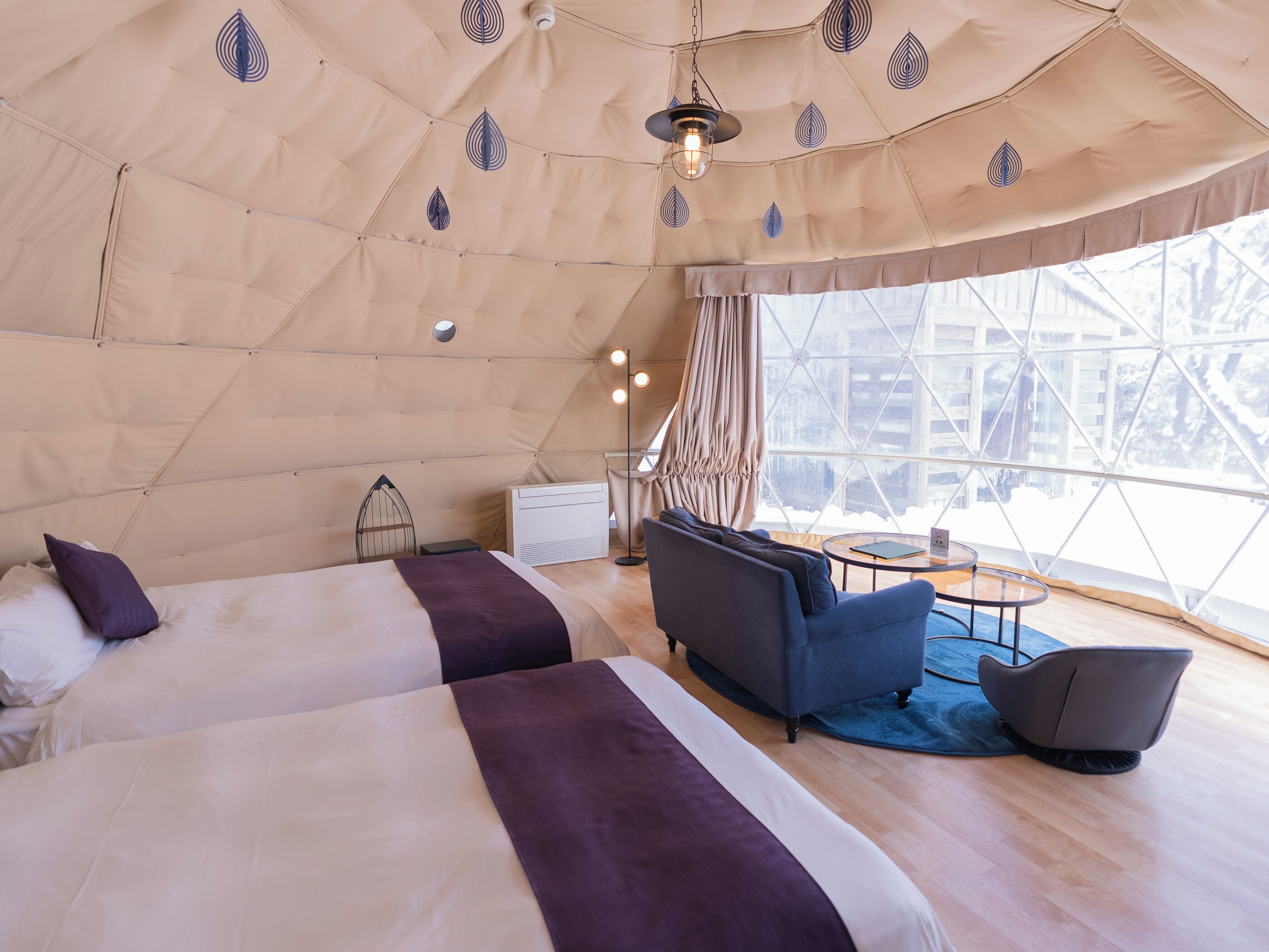 A tent-style room with two beds, a sofa, a small table, and a chair.