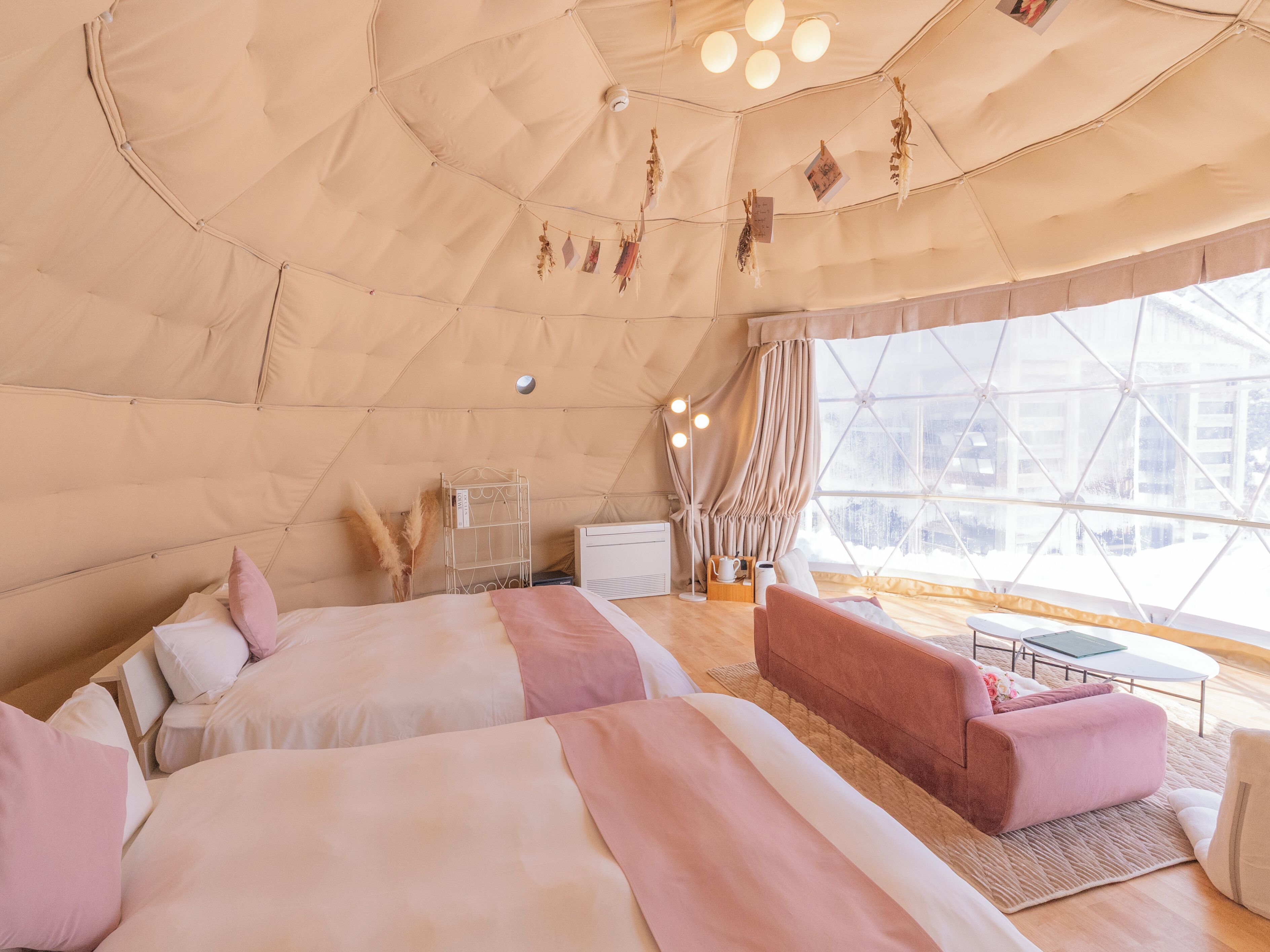A tent-style room with two beds, a sofa, a small table, and a window with a view of buildings.