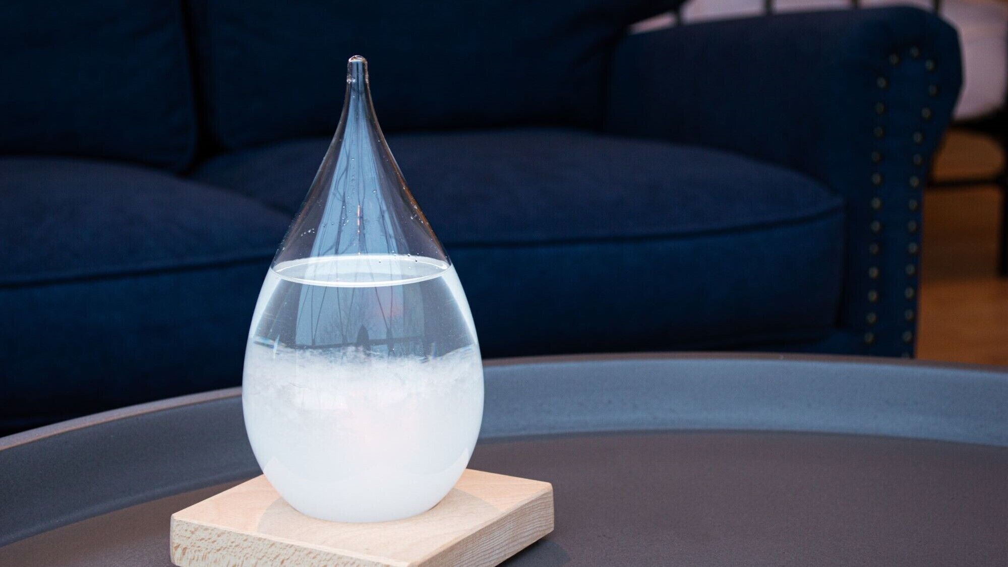 A clear glass vase with water on a wooden coaster on a round table.