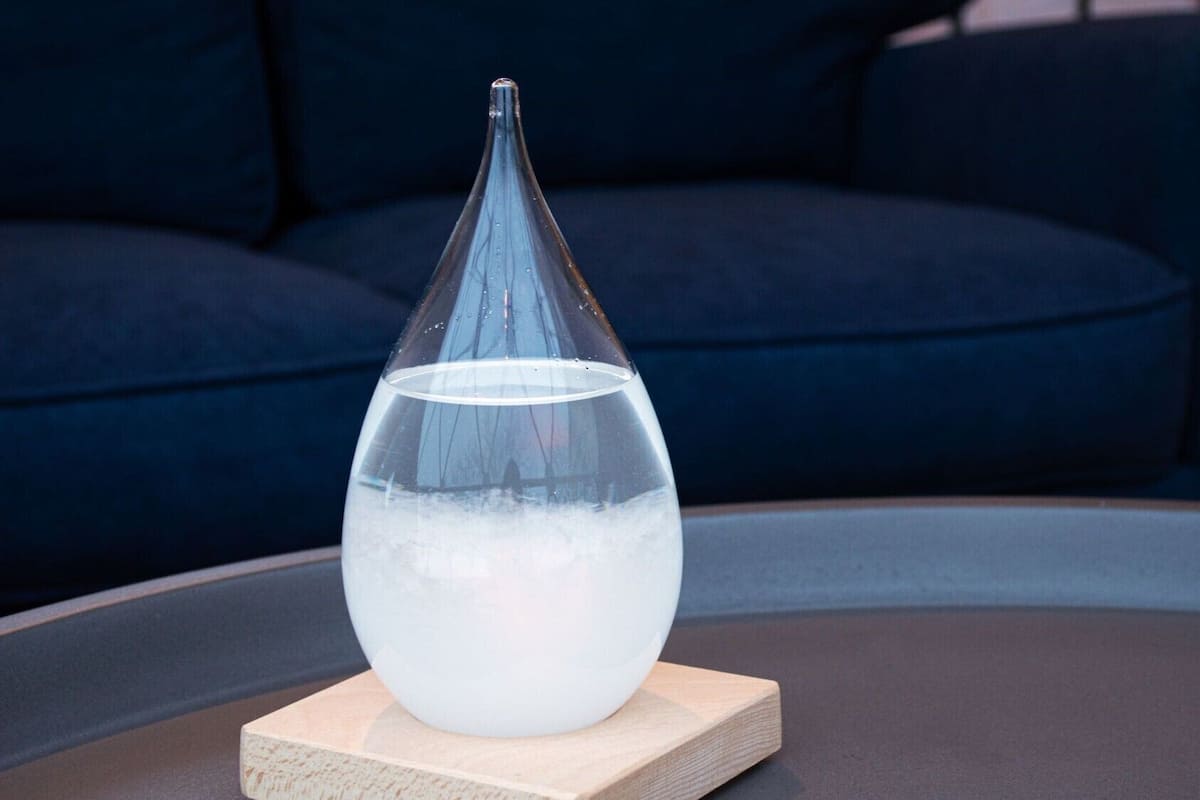 A clear glass vase with water on a wooden coaster on a round table.
