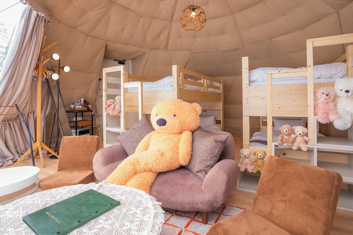 A tented accommodation with bunk beds, a large teddy bear, and a cozy seating area.