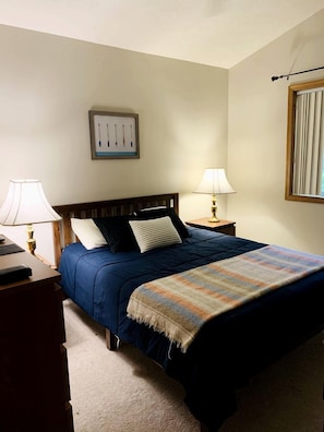 A hotel room with a bed, two bedside lamps, a nightstand, a framed picture on the wall, and a window with blinds.