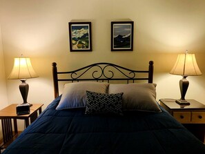 Un lit avec une tête de lit, deux tables de chevet avec des lampes et deux tableaux encadrés accrochés au mur.