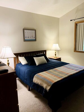 A hotel room with a bed, two bedside lamps, a nightstand, a framed picture on the wall, and a window with blinds. - Lake Cabin with Hot-Tub and Deck in Pennsylvania (Lake Ariel)