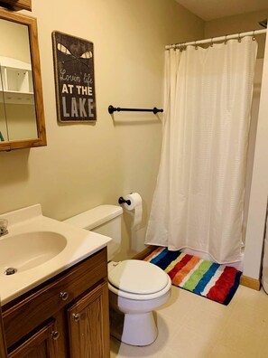 A bathroom with a toilet, sink, mirror, and a shower curtain. - Lake Cabin with Hot-Tub and Deck in Pennsylvania (Lake Ariel)
