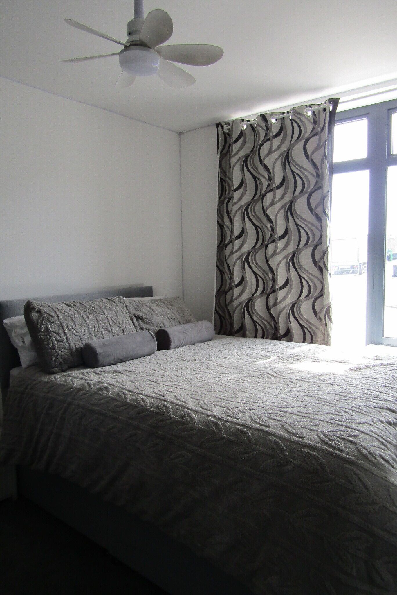 Une chambre à coucher avec un lit, un ventilateur de plafond et une fenêtre avec des rideaux.