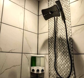 Una ducha con cabezal de ducha manual, panel de control con varias configuraciones y pared cubierta de azulejos.