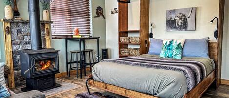 A cozy bedroom with a bed, a fireplace, a desk, and a hanging shelf.