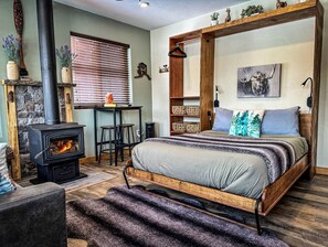 A cozy bedroom with a bed, a fireplace, a desk, and a hanging shelf.