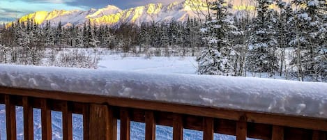 A snowy mountain landscape with a wooden deck in the foreground.