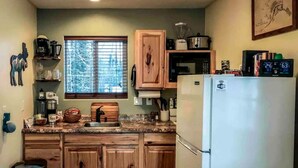 Une cuisine avec des meubles de rangement en bois, un réfrigérateur, une fenêtre avec des stores et divers appareils de cuisine.