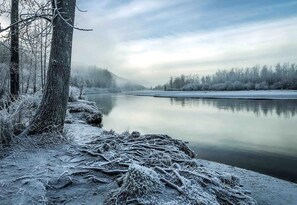 A serene winter landscape with a frozen river, bare trees, and a misty background.