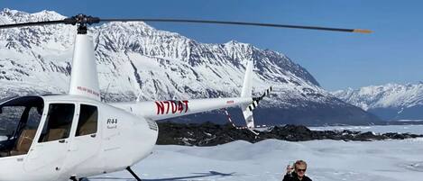 A helicopter with a person sitting on the snow beside it.