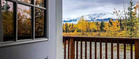 A view from a window with a wooden deck, a mountain range, and autumn foliage.