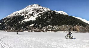 Eine verschneite Landschaft mit einem Berg und zwei Radfahrern.
