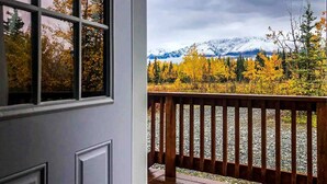 Une vue depuis une fenêtre donnant sur une terrasse en bois, une chaîne de montagnes et le feuillage automnal.