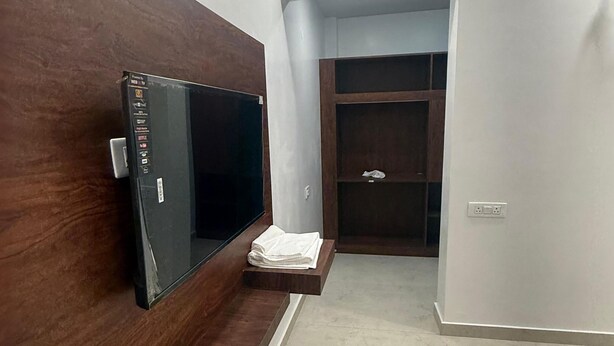 Een gang met een houten bankje, een flatscreen televisie aan de muur, een witte handdoek op een plank en een kast met een spiegel.