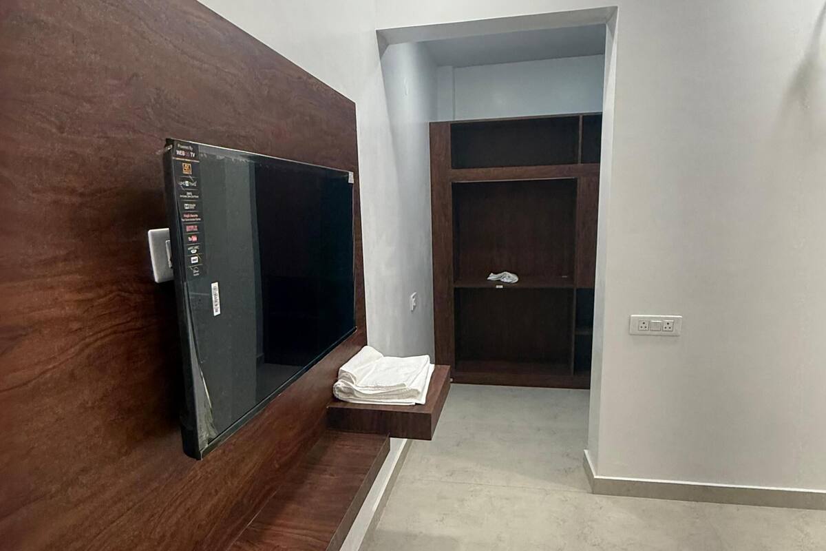 A hallway with a wooden bench, a flat-screen TV mounted on the wall, a white towel on a shelf, and a closet with a mirror.