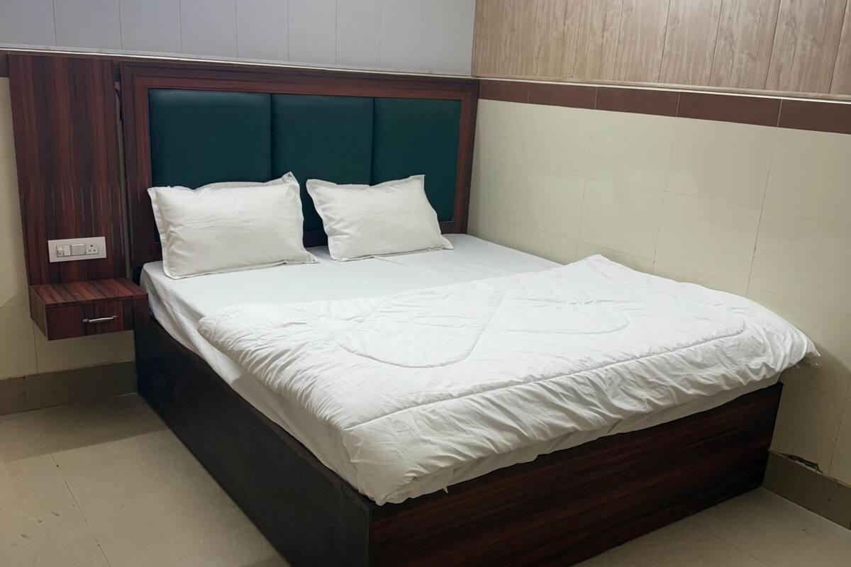 A neatly made bed with white linens, a wooden headboard, and a bedside table with a power outlet.