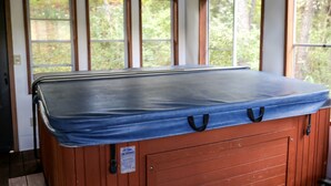 A hot tub with a blue cover, wooden walls, and multiple windows with a view of trees. - Family-Friendly Cabin Rental on a Private Lake near Wisconsin Dells (Tomah)
