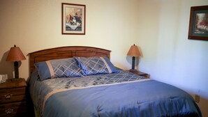 A bedroom with a wooden headboard, a blue bedspread, two bedside lamps, and a framed picture on the wall. - Family-Friendly Cabin Rental on a Private Lake near Wisconsin Dells (Tomah)