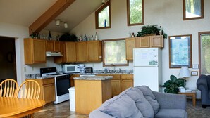 A kitchen with wooden cabinets, a stove, microwave, and refrigerator; a dining area with a table and chairs; and a living area with a sofa. - Family-Friendly Cabin Rental on a Private Lake near Wisconsin Dells (Tomah)