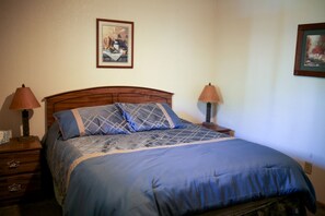 Un dormitorio con cabecera de madera, colcha azul, dos lámparas de noche y un cuadro en la pared.