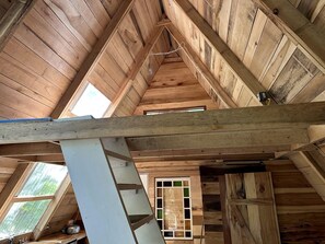 Un interior de madera con techo inclinado, una ventana con vidrio verdoso y una estructura de vigas blancas.