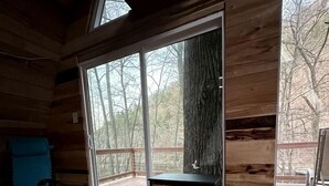 Un interior de cabaña acogedor, con una estufa de leña, ventanas amplias y un sillón azul.