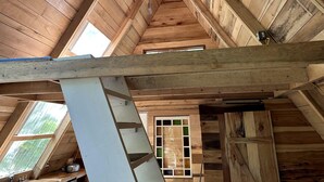 Un interior de madera con techo inclinado, una ventana con vidrio verdoso y una estructura de vigas blancas.