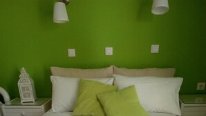 A neatly made bed with a swan towel arrangement, green pillows, and a white nightstand with a decorative lantern. - Evizorzia Villas -Olive Tree Green Villa (Santorini)