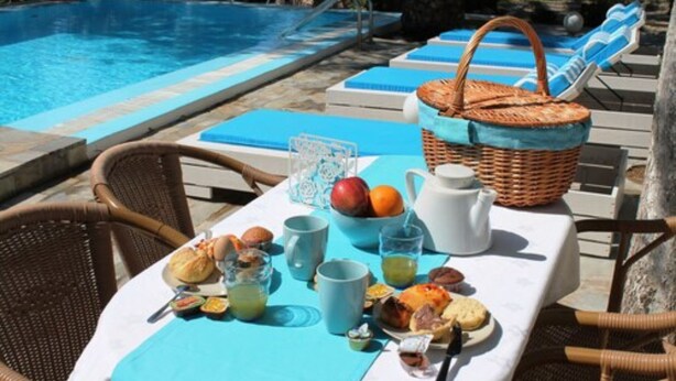 A poolside breakfast setup with lounge chairs, a table with food and drinks, and a wicker basket. - Evizorzia Villas -Olive Tree Green Villa (Santorini)