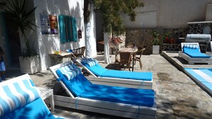 A poolside area with sun loungers, a table with chairs, and a stone wall. - Evizorzia Villas -Olive Tree Green Villa (Santorini)