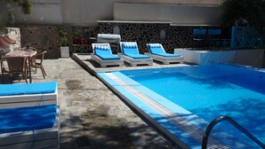 A swimming pool with lounge chairs, a table, and a stone wall. - Evizorzia Villas -Olive Tree Green Villa (Santorini)