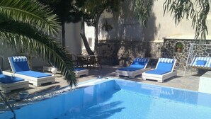 A pool area with lounge chairs and a stone wall. - Evizorzia Villas -Olive Tree Green Villa (Santorini)