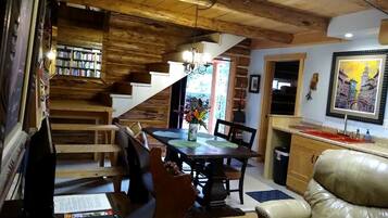 Una sala de estar acogedora con una mesa de comedor, sillas de cuero, una estantería y una escalera que sube a otro nivel.