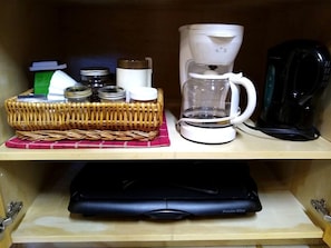 Une étagère de cuisine avec une machine à café, un panier rempli de bocaux et un appareil Proctor Silox.