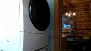 Lavadora y secadora apiladas en una habitación con paredes de madera y una lámpara de araña.