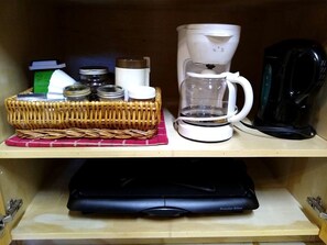 Une étagère de cuisine avec une machine à café, un panier rempli de bocaux et un appareil Proctor Silox.