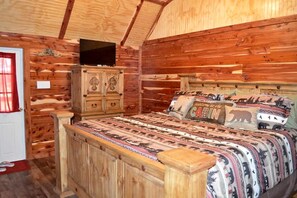 Interior de una cabaña de madera con una cama, un televisor y un armario.