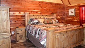 A cabin-style bedroom with a wooden headboard, a bed with patterned bedding, a nightstand, and a cabinet. - Secluded Getaway on a Vineyard in Allen, Oklahoma (Allen)