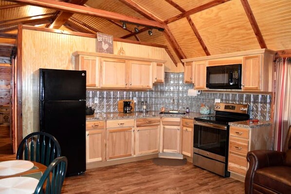 Une cuisine avec des meubles de rangement en bois, un réfrigérateur noir, un four à micro-ondes et une cuisinière.