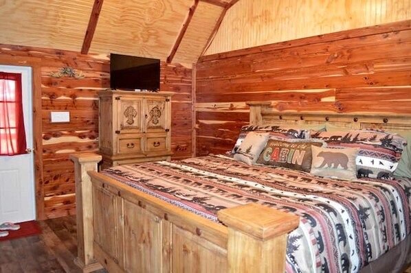 A wooden cabin interior with a bed, a television, and a cabinet.