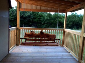 Une terrasse en bois avec une balançoire, entourée d’une rambarde en bois, et une vue sur les arbres en arrière-plan.