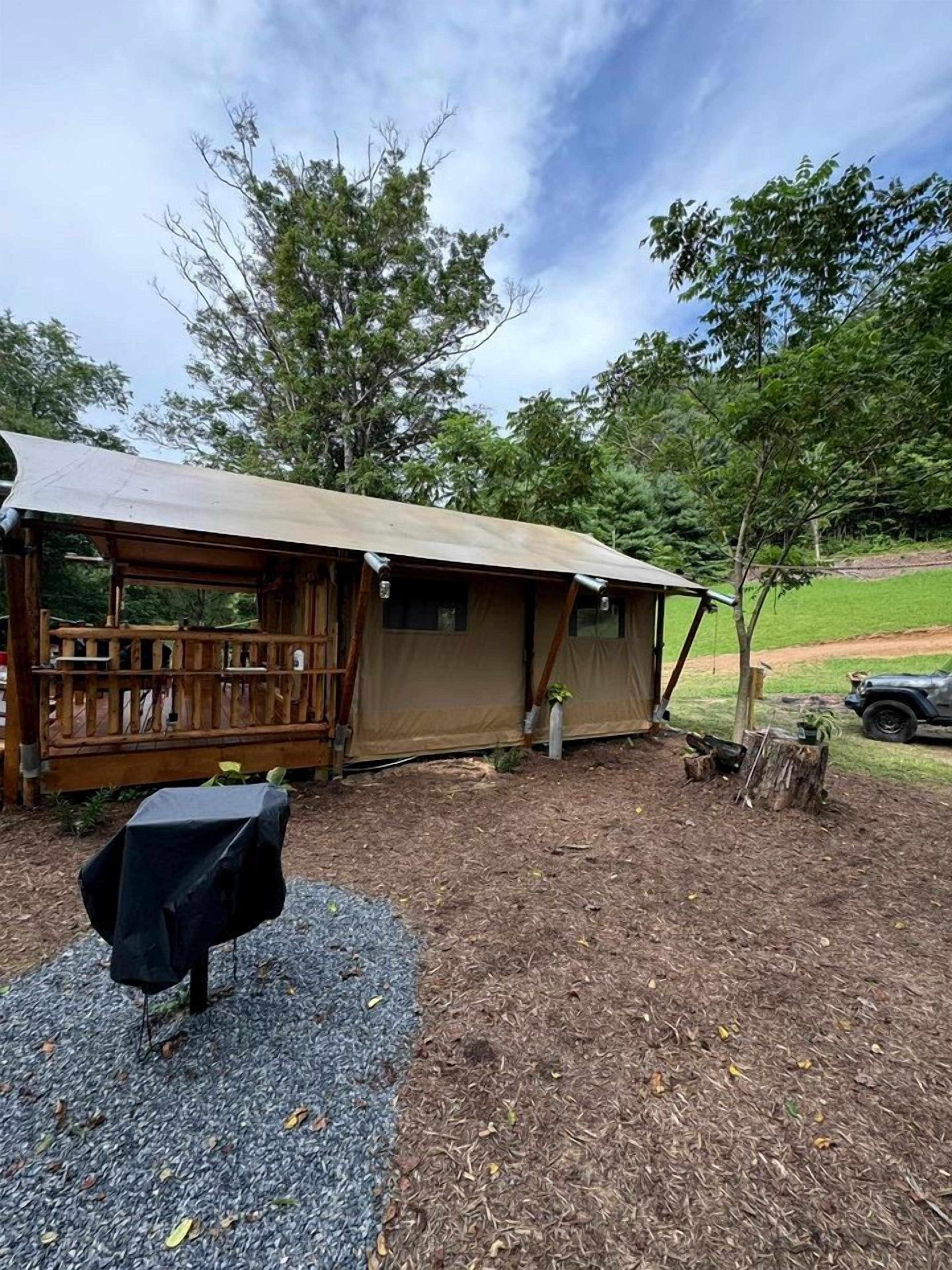 A rustic cabin with a covered porch, a small table with a black tablecloth, and a gravel area.